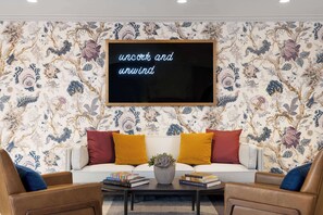 A living room with a floral wallpaper, a blackboard with text, a white sofa, and two brown armchairs.