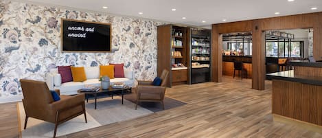 A modern living room with a sofa, armchairs, a coffee table, and a TV. There is a bookshelf and a bar area visible through an open doorway.