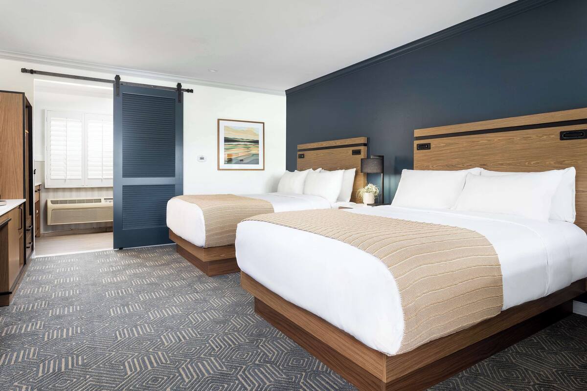 A hotel room with two beds, a large window, a sliding door, and a view of the outdoors.