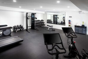 A modern gym with a treadmill, stationary bikes, weight machines, and a mirror reflecting the equipment.