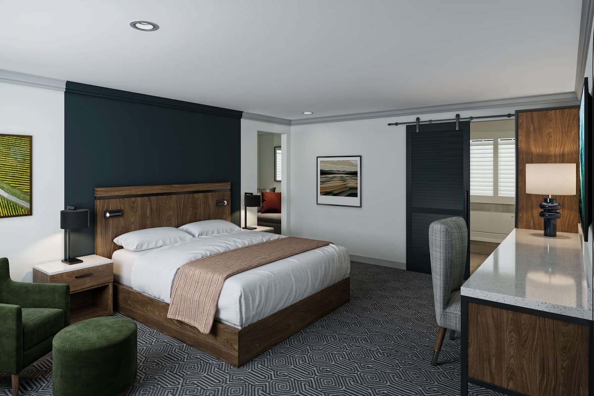 A modern hotel room with a large bed, a green armchair, a desk with a lamp, and a view of the outdoors.