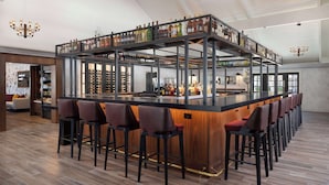 Zona de bar moderna con una isla central, diversas opciones de asientos y una variedad de botellas exhibidas en estantes.