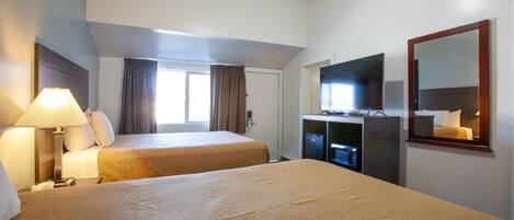 A hotel room with two beds, a desk with a computer, a mirror, and a window with curtains.