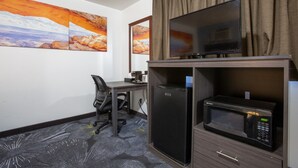 Habitación de hotel con escritorio, silla, refrigerador, microondas y televisión de pantalla plana.