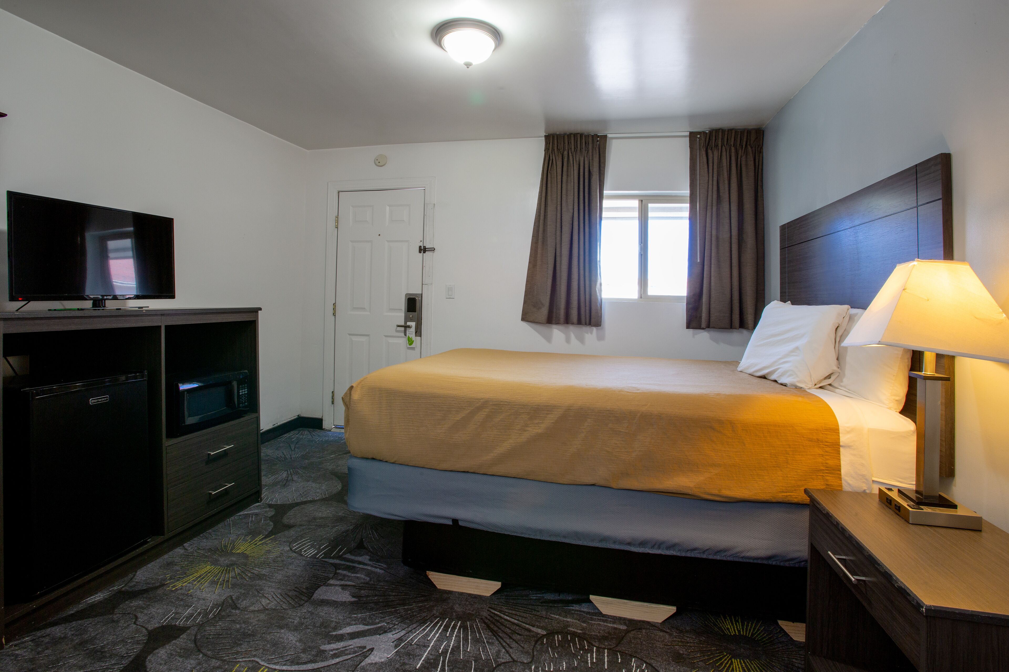 Een hotelkamer met een bed, een televisie, een bureau met een computer en een lamp.