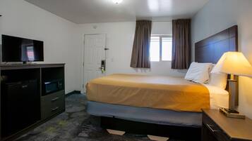 Een hotelkamer met een bed, een televisie, een bureau met een computer en een lamp.