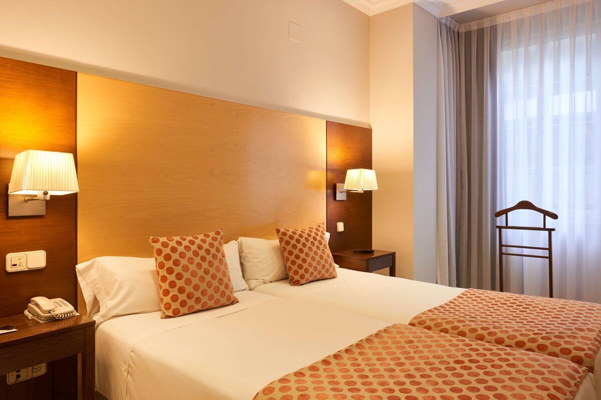Habitación de hotel con una cama doble, dos lámparas de noche, un teléfono y cabecero de madera.