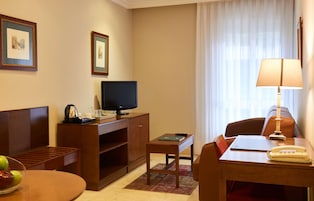 Ein Hotelzimmer mit einem Bett, einem Fernseher, einem Schreibtisch mit Lampe, einem Telefon und einem kleinen Tisch mit einer Obstschale.
