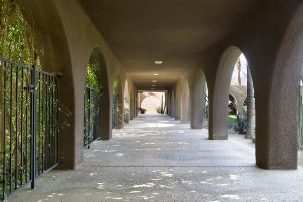 Un pasaje cubierto con arcos, suelo de hormigón y una valla metálica a un lado.