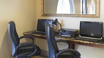 Un espacio de trabajo con dos sillas de oficina negras, un escritorio con dos computadoras portátiles, una impresora y un espejo grande en la pared.