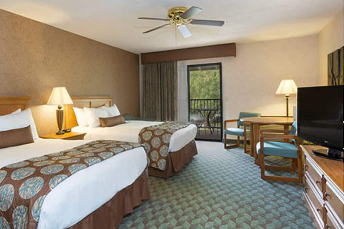 A hotel room with two beds, a ceiling fan, a TV, and a balcony with a view.