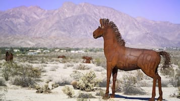 Una gran estatua de un caballo color óxido en un paisaje desértico con montañas al fondo.