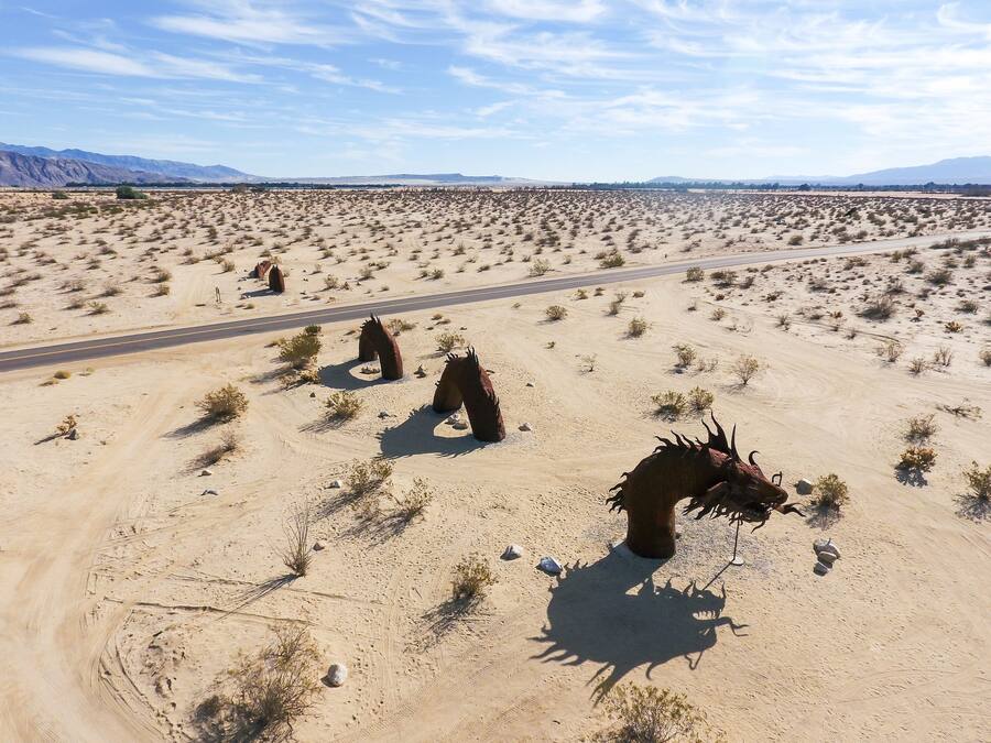 Paisaje desértico con una carretera y estatuas de caballos.