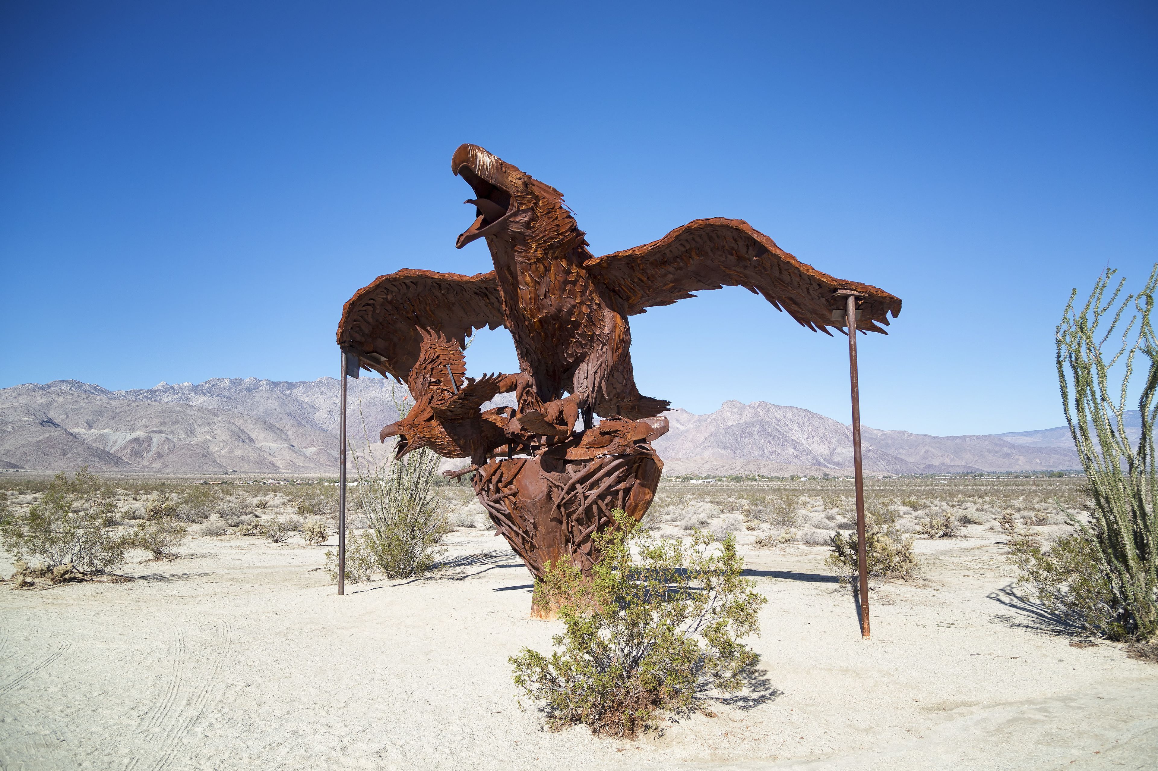 Una gran escultura de metal de un pájaro en un paisaje desértico con montañas al fondo.