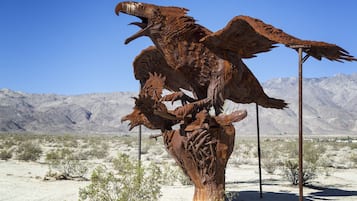 A large metal sculpture of a bird in a desert landscape with mountains in the background.