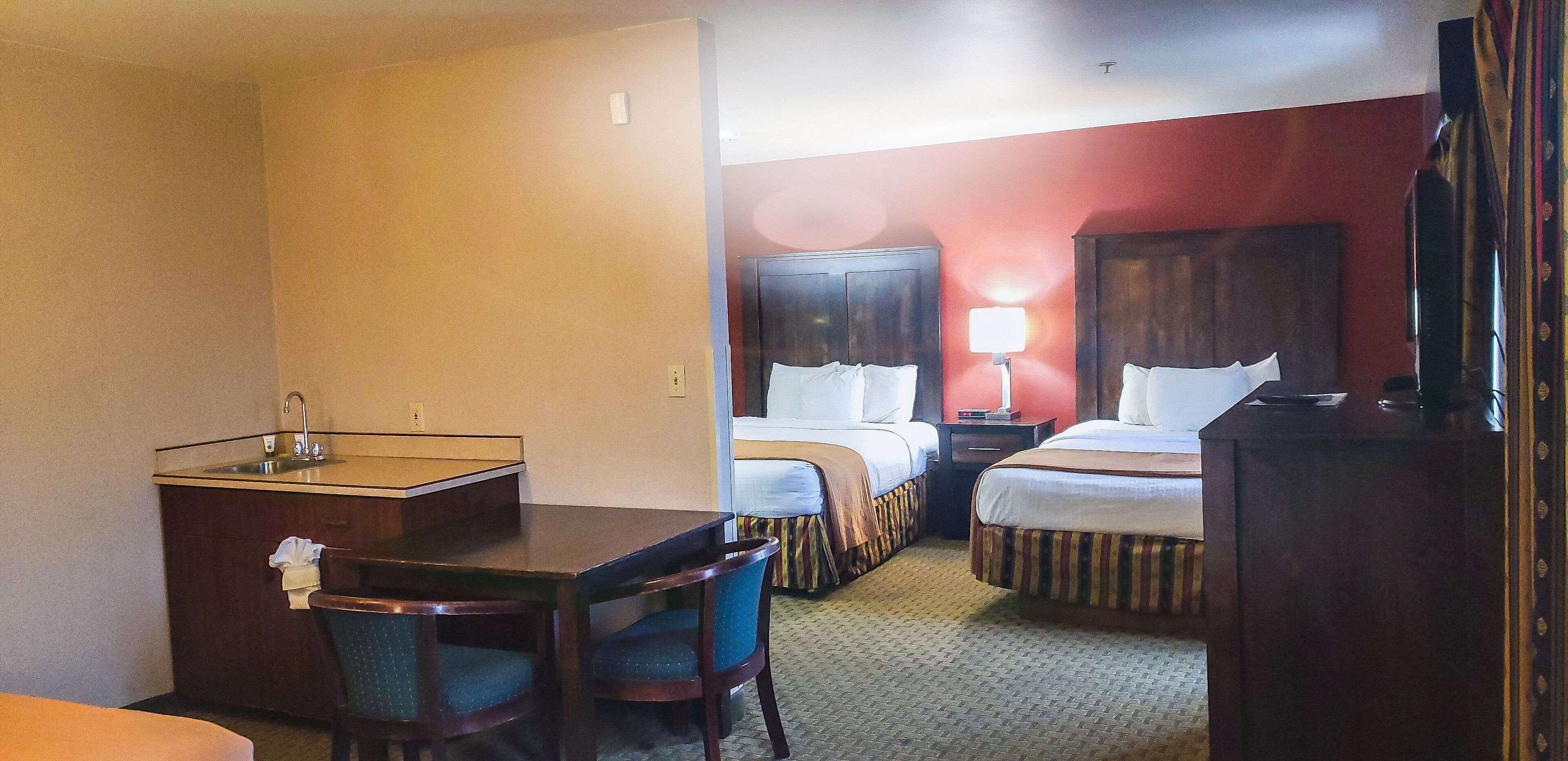 A hotel room with a desk, two beds, a nightstand, a lamp, and a TV.