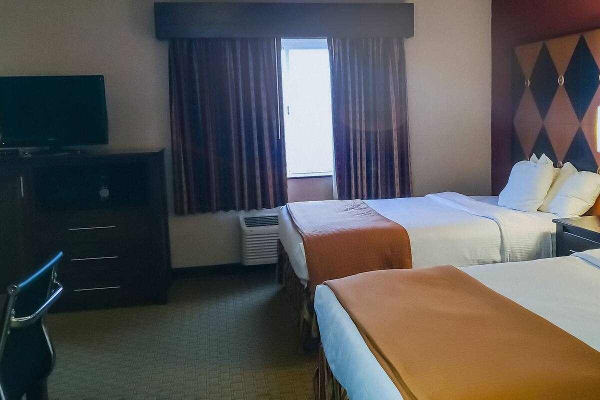 A hotel room with two beds, a desk with a TV, a chair, and a window with curtains.