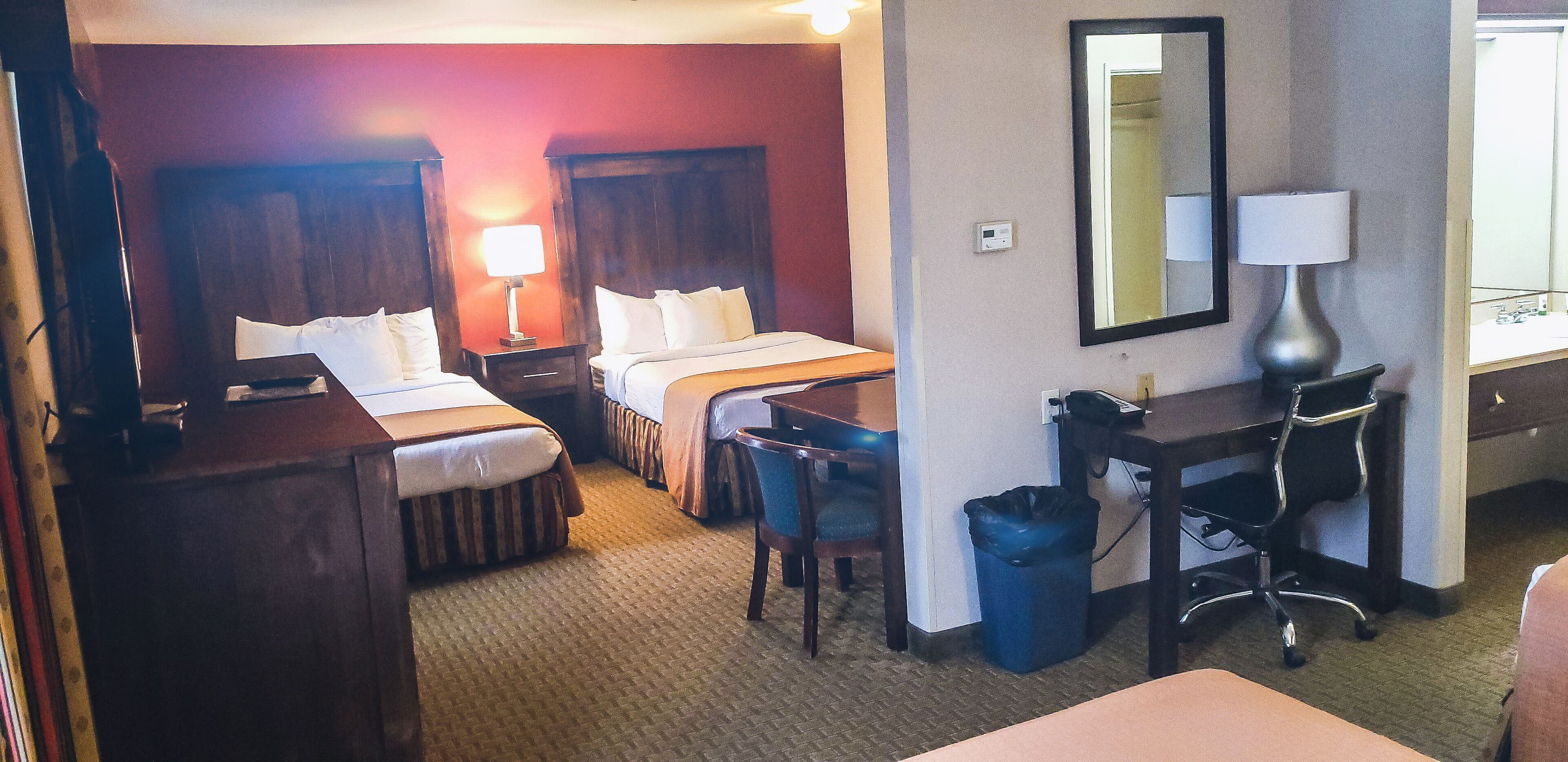 A hotel room with two beds, a desk, a chair, a trash bin, and a mirror.