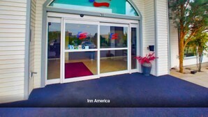 The exterior of an Inn America building with a large arched entrance, a red carpet, and a potted plant. - Inn America - Lewiston (Lewiston)