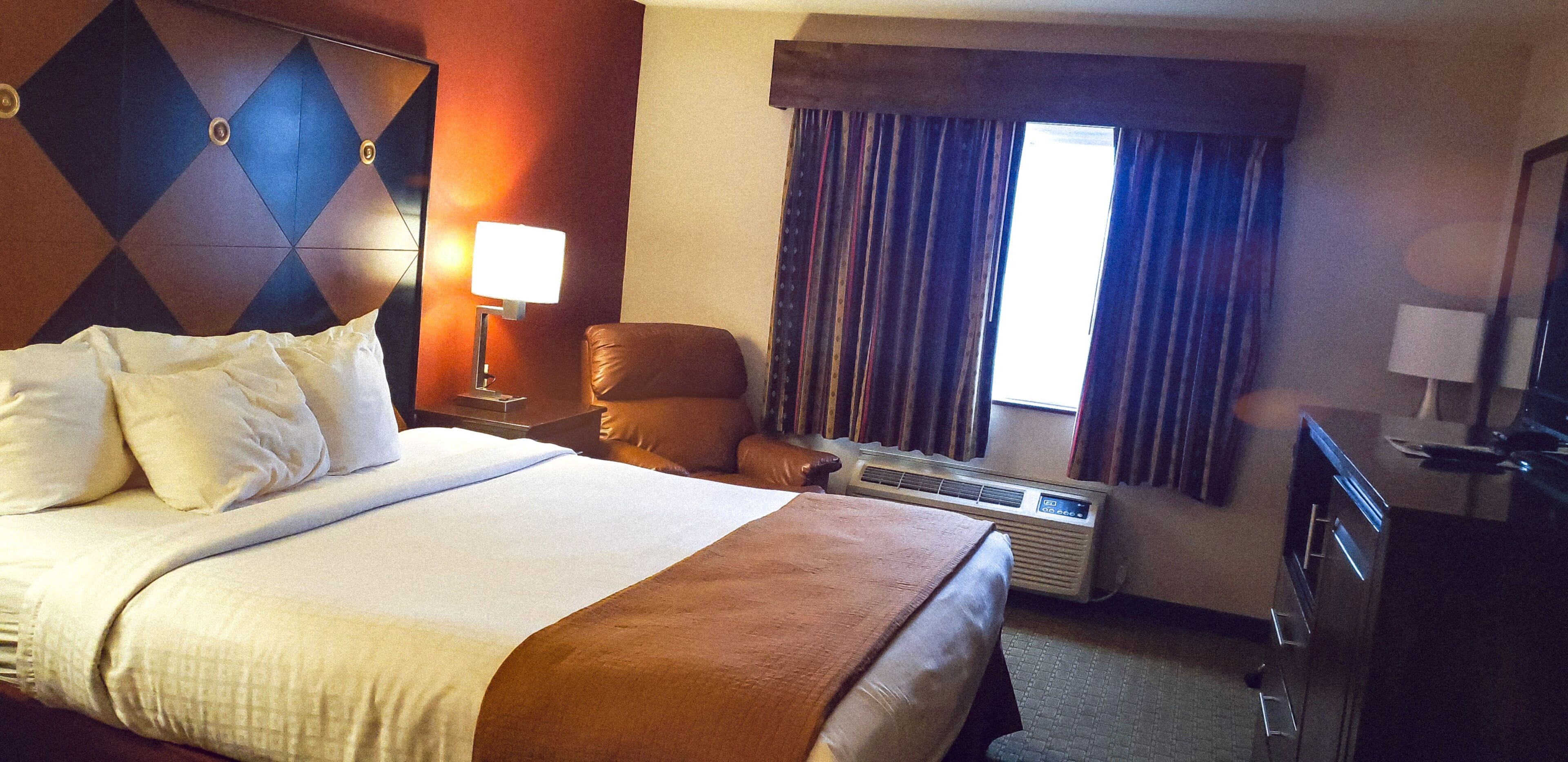 Una habitación de hotel con una cama grande, una silla, un escritorio y un ventanal con cortinas.