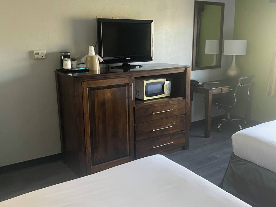 Habitación de hotel con cama, cómoda de madera con televisor, microondas y escritorio con silla.