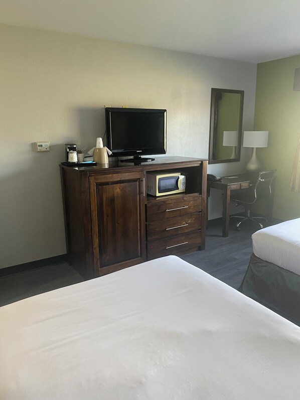 A hotel room with a bed, a wooden dresser with a television, a microwave, and a desk with a chair.