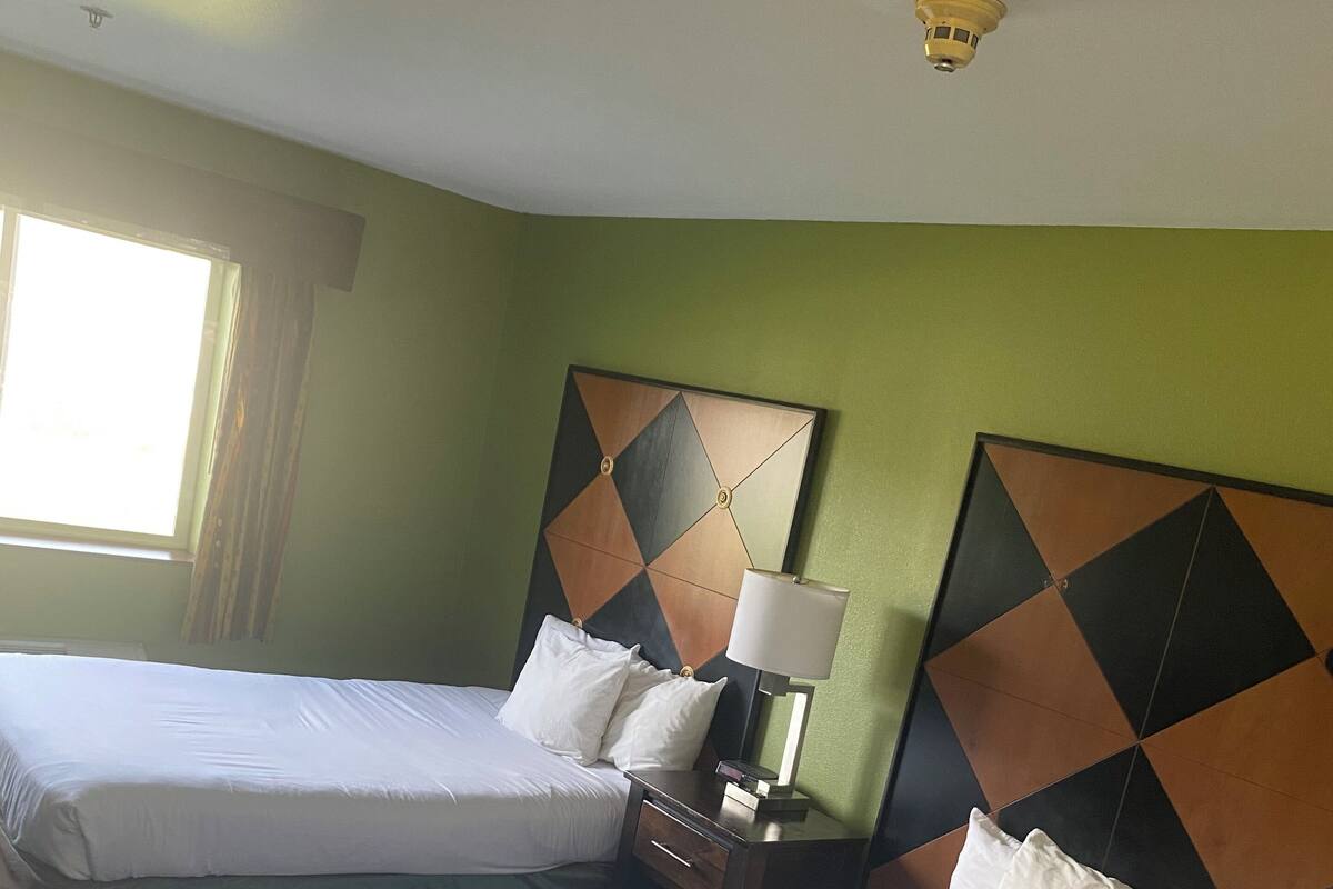 A hotel room with two beds, a nightstand with a lamp, and a window with curtains.