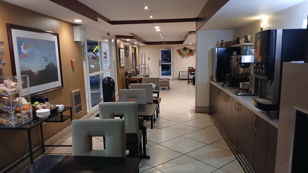A hotel lobby with a dining area, a coffee station, and a large screen displaying a scenic view. - Inn America - Lewiston (Lewiston)