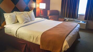 A hotel room with a large bed, a nightstand, a lamp, a chair, and an air conditioning unit.