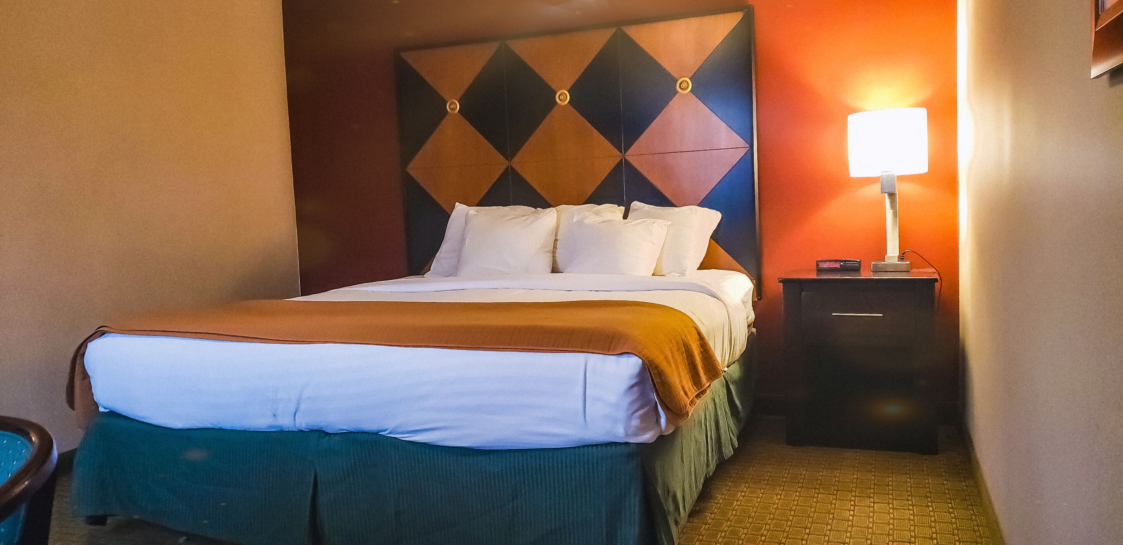 Hotellihuone, jossa on sänky, yöpöytä lampun kanssa ja kuviollinen seinä.