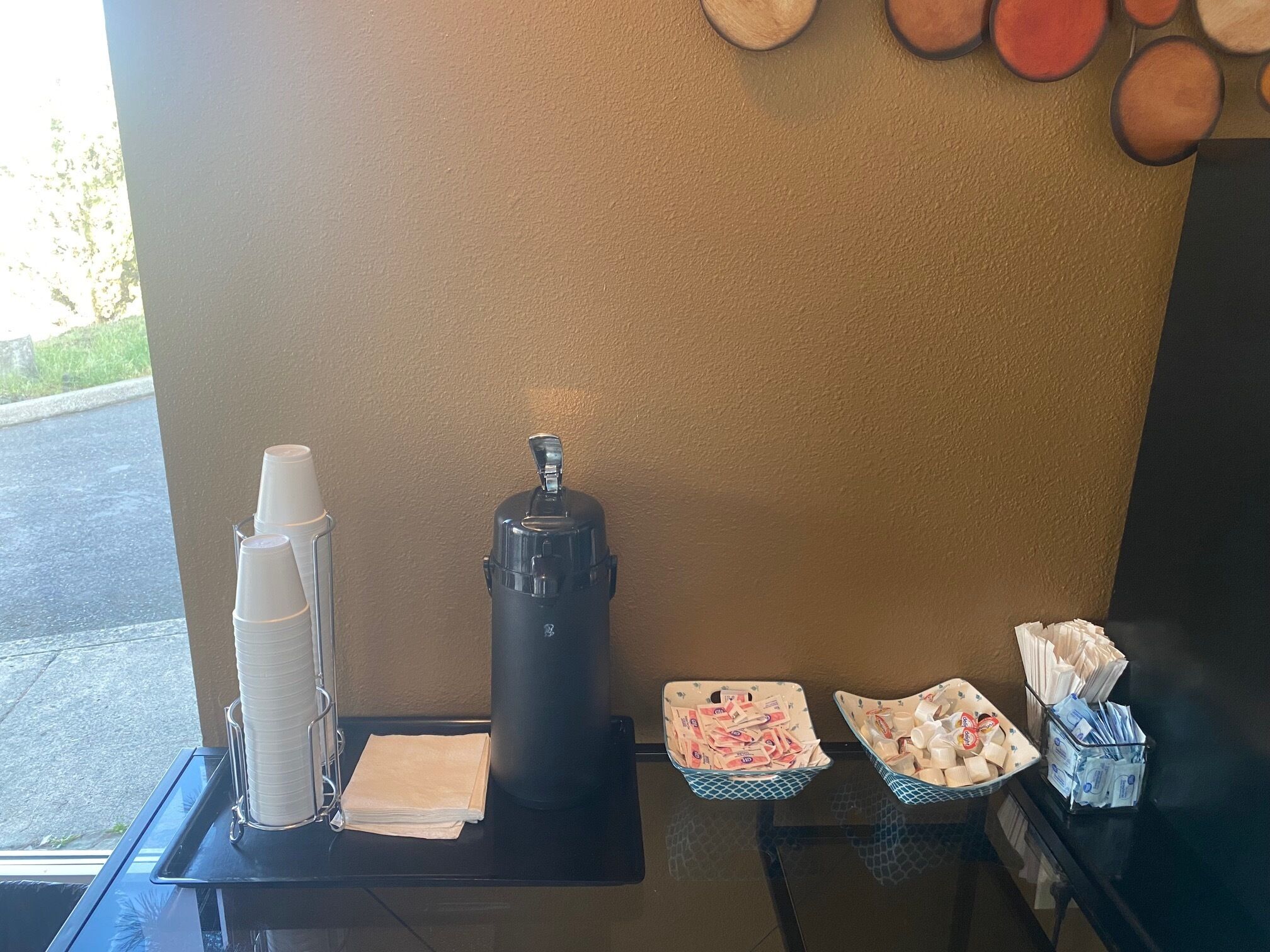 A coffee station with a coffee maker, cups, napkins, and condiments.