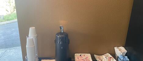 A coffee station with a coffee maker, cups, napkins, and condiments.