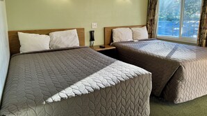 A hotel room with two beds, each with a quilted bedspread, a wooden headboard, and a nightstand with a telephone. - Snoozinn (Wilsonville)