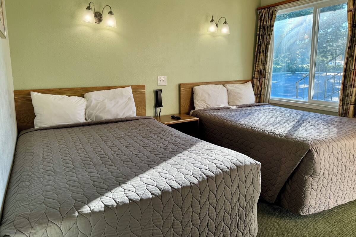 A hotel room with two beds, each with a quilted bedspread, a wooden headboard, and a nightstand with a telephone.