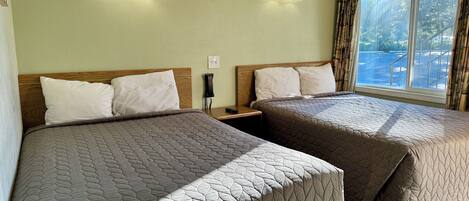 Habitación de hotel con dos camas, cada una con colcha acolchada, cabecero de madera y mesita de noche con teléfono.