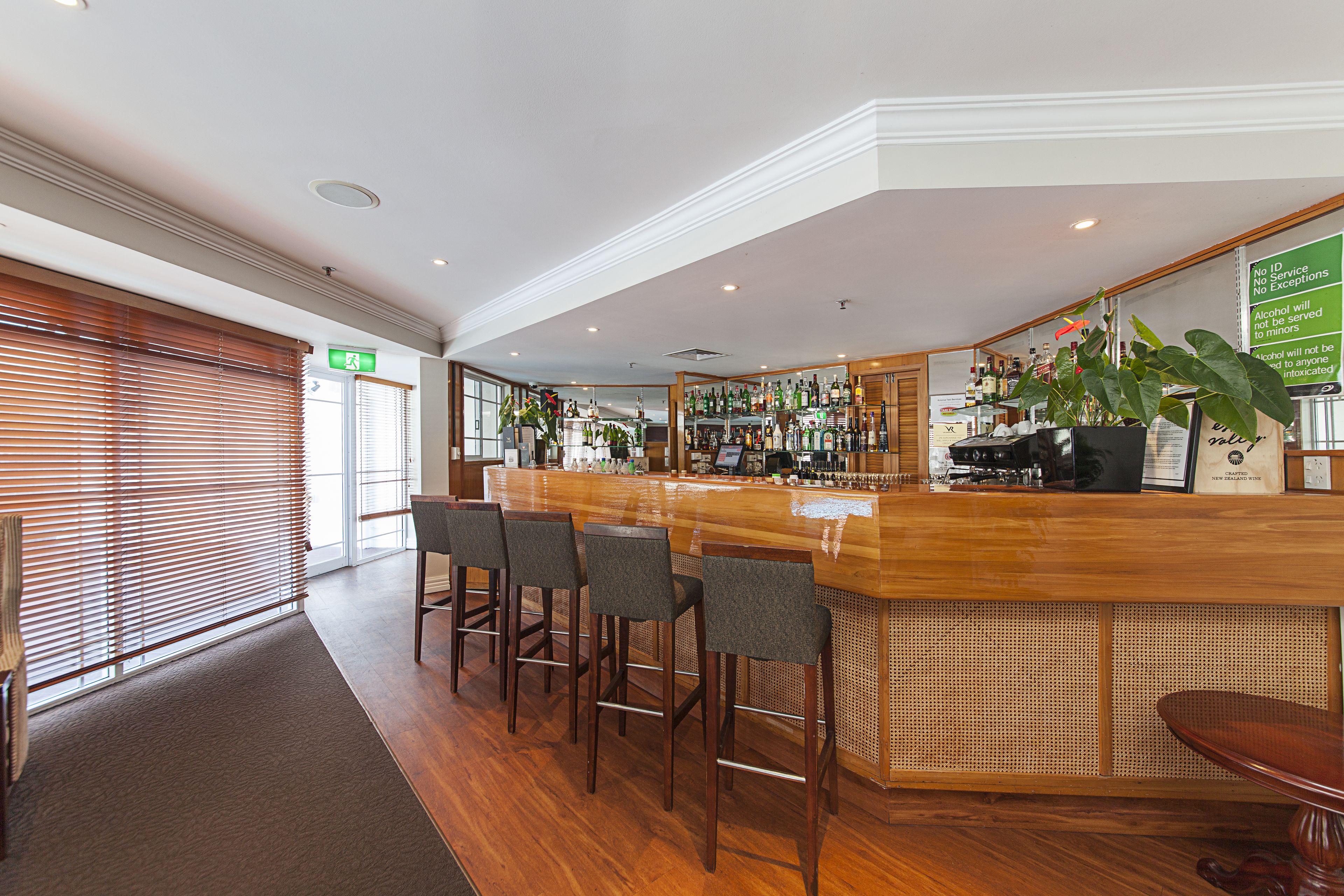 A bar area with wooden bar stools, a counter with a cash register, and a variety of bottles and glasses.