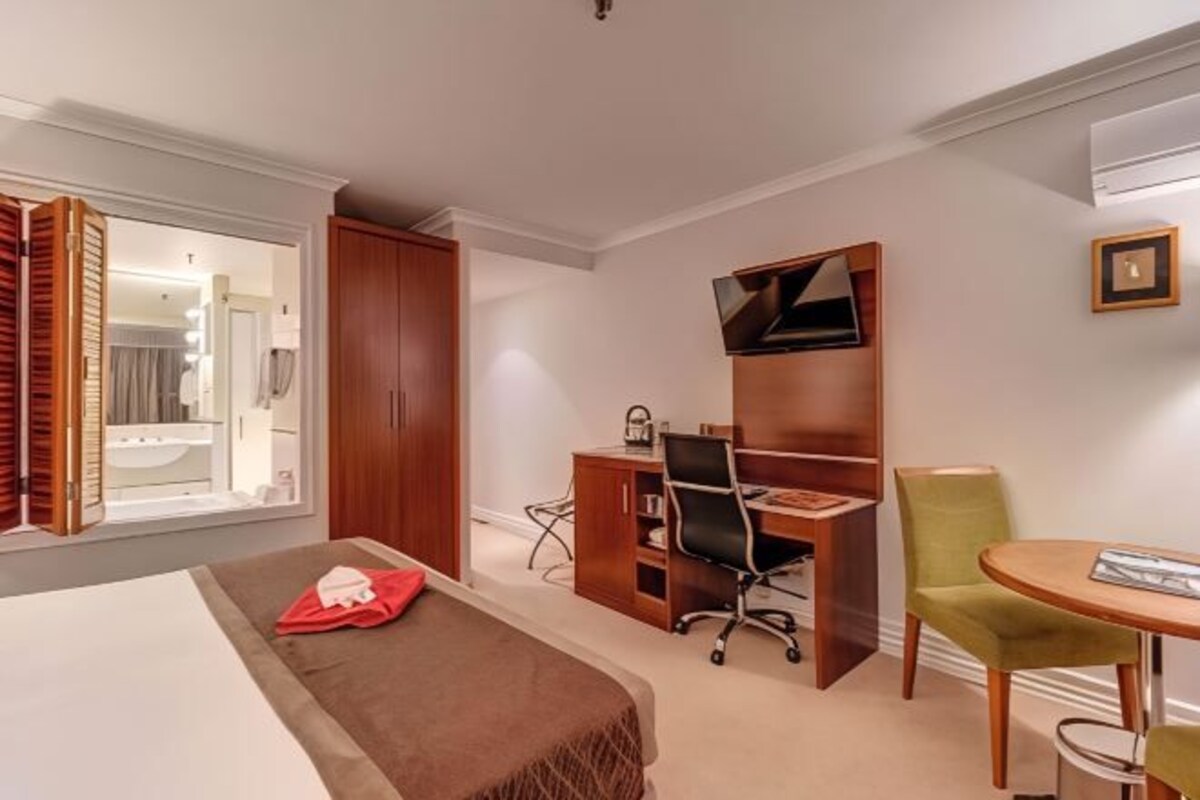 Habitación de hotel con cama, escritorio, silla y una mesita.