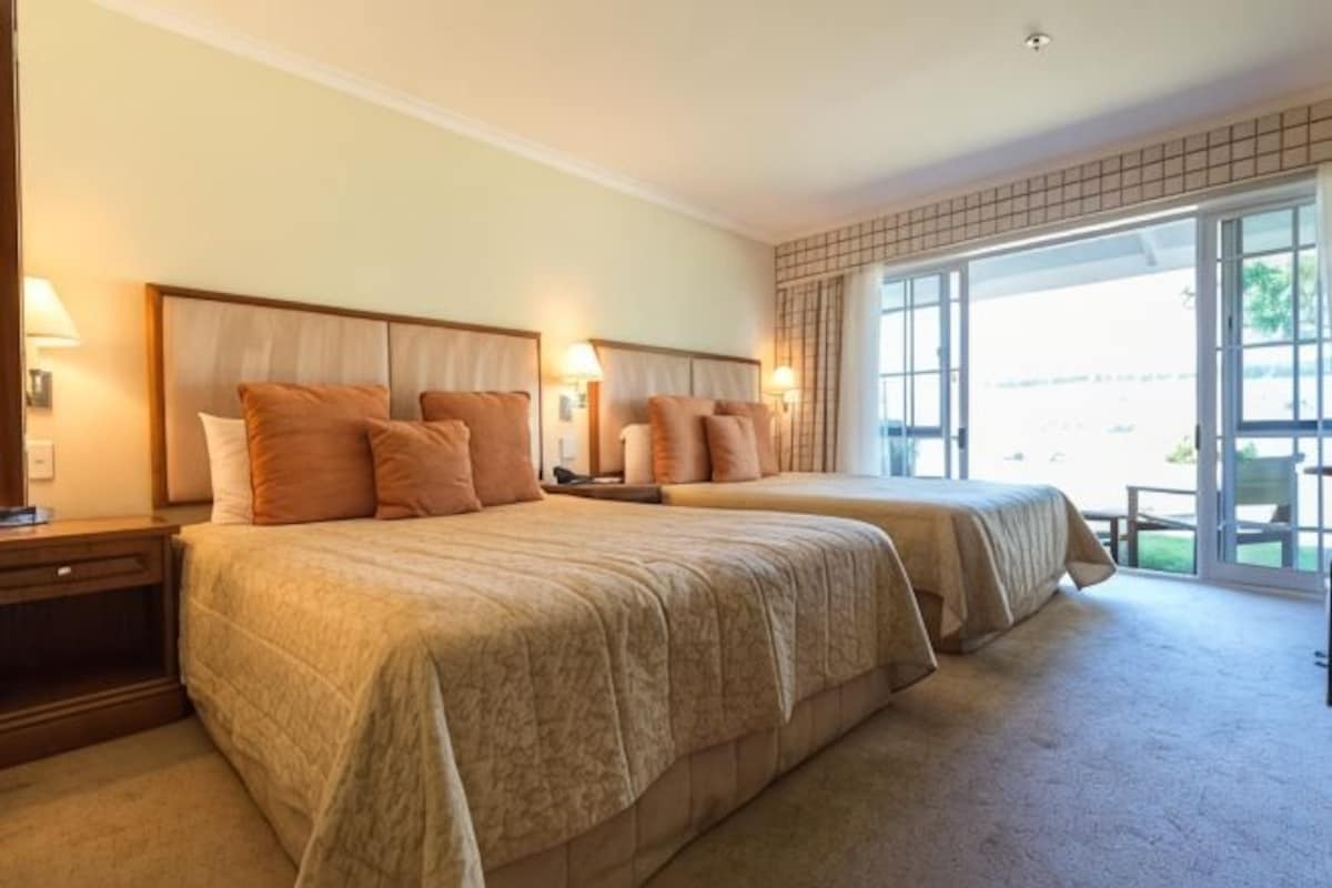 Habitación de hotel con dos camas, un ventanal grande y vistas al exterior.