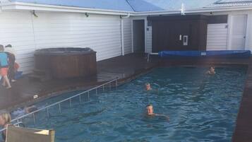 A swimming pool with a wooden deck, a hot tub, and a covered area with a roof.