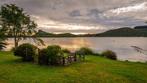 Une vue sur le lac, avec un pont en bois, des zones herbeuses et des collines en arrière-plan.