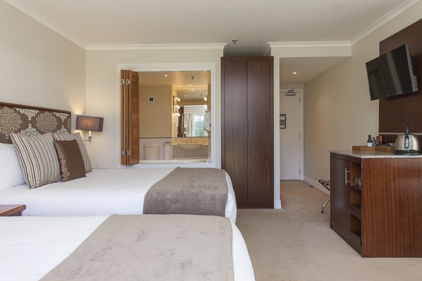 Ein Hotelzimmer mit zwei Betten, einem Holzschrank, einem Fernseher und einem durch eine offene Tür einsehbaren Badezimmer.
