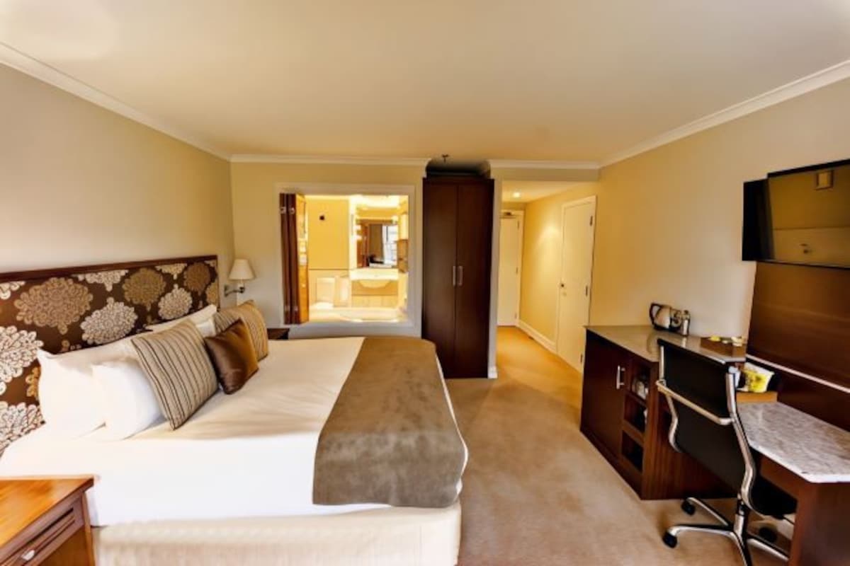 A hotel room with a large bed, a desk, and a wardrobe.