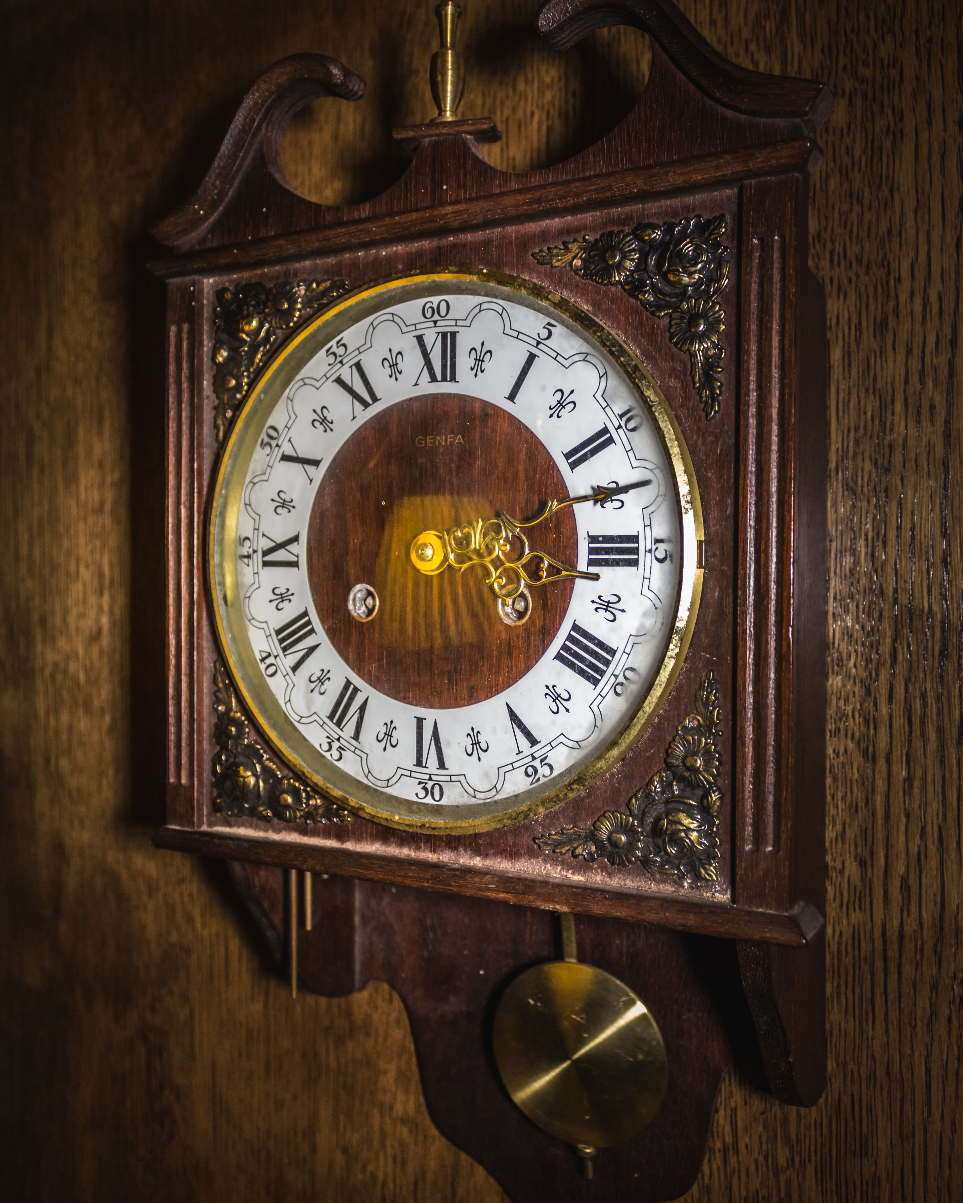 A detailed view of a wooden wall clock with Roman numerals and a pendulum mechanism.