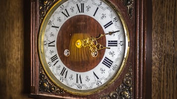 A detailed view of a wooden wall clock with Roman numerals and a pendulum mechanism.