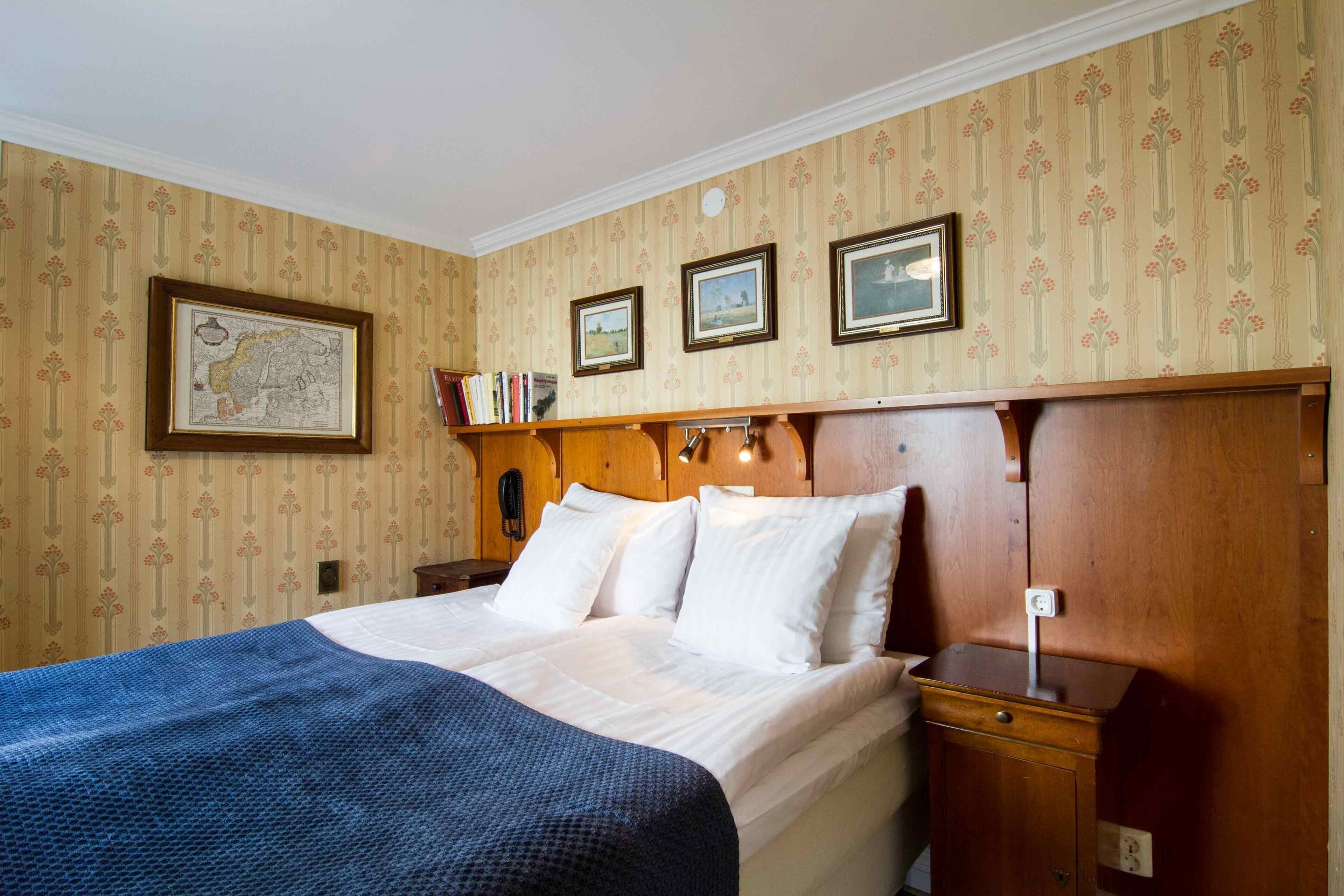 A neatly made bed with a blue blanket, a wooden nightstand with a lamp, and a wall with three framed pictures.