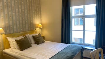 Een hotelkamer met een bed, twee bedlampen, een raam met gordijnen en een radiator.
