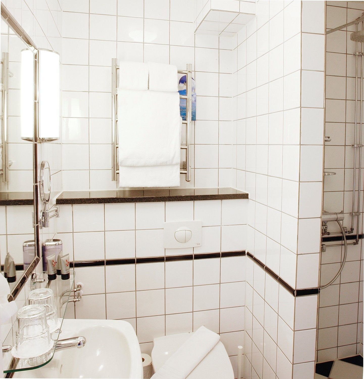 A bathroom with white tiles, a sink, a mirror, a towel rack, and a shower area.