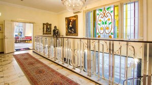 A grand hallway with a marble floor, a chandelier, a red carpet, and a view of the street outside. - Mayfair Hotel Tunneln (Malmö)