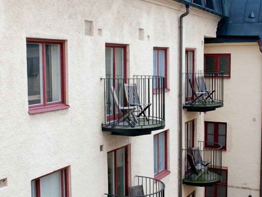 Un edificio de varios pisos con balcones, cada uno con una silla y una mesita.