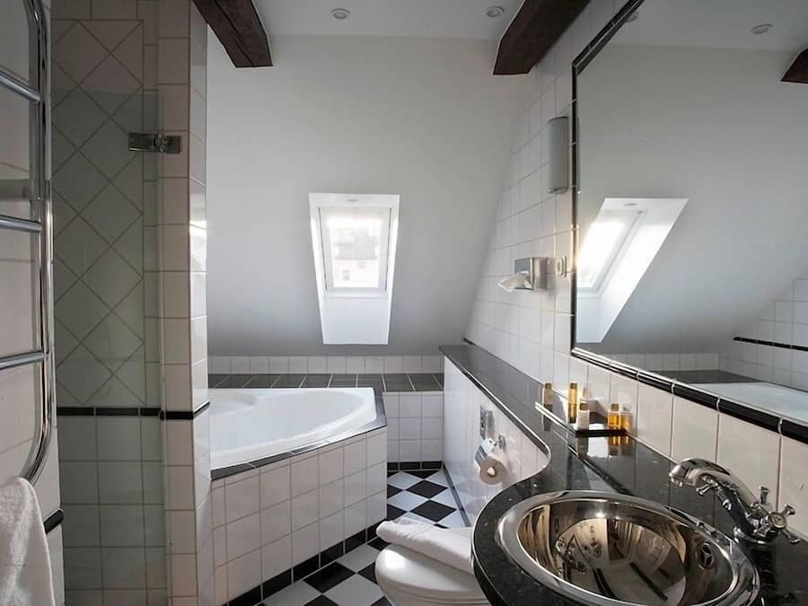 A modern bathroom with a black and white checkered floor, a freestanding bathtub, a toilet, and a large mirror with a skylight above.